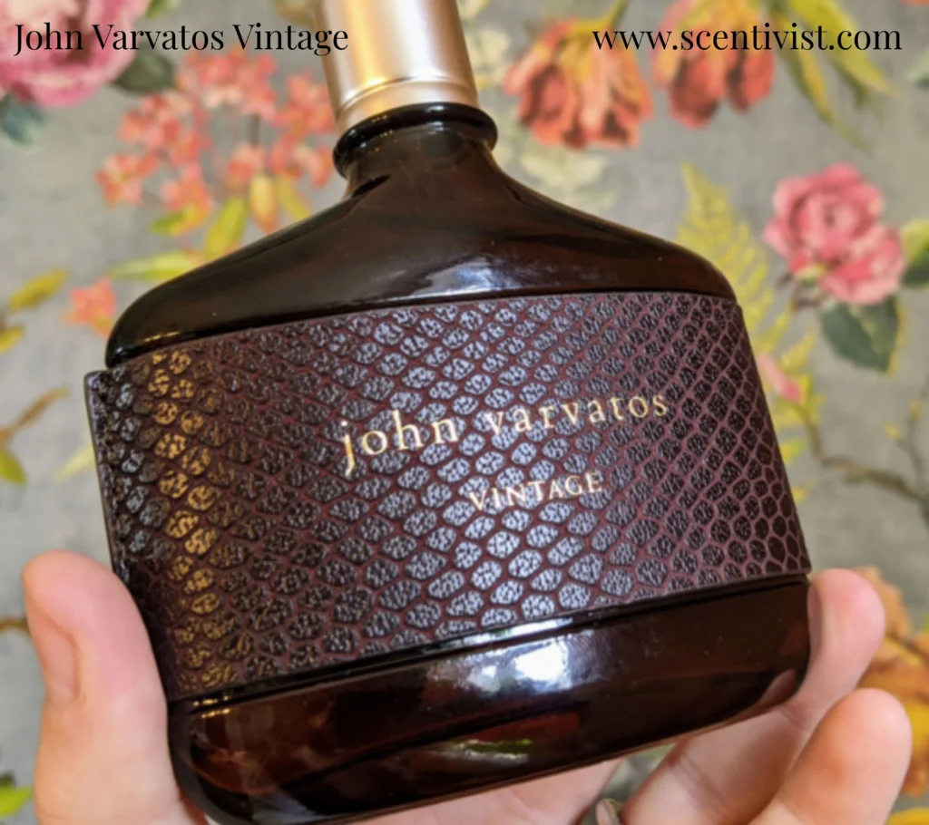 Hand holding John Varvatos Vintage Eau de Toilette bottle with brown leather-textured wrap and gold cap.