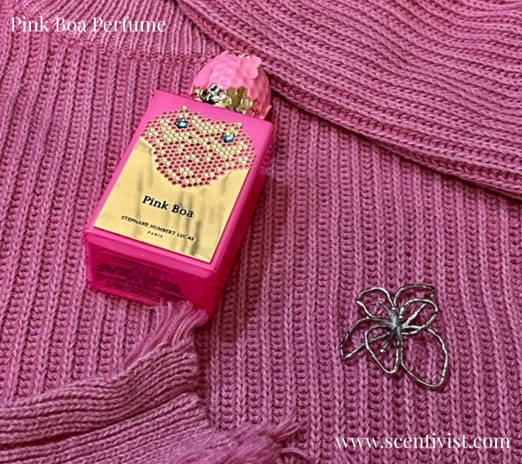 Pink Boa perfume bottle resting on a soft pink jersey, showcasing its elegant curved design and gold-accented cap.