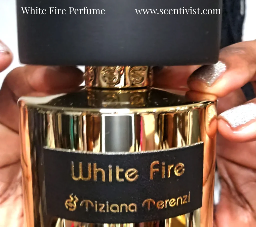 Close-up of White Fire perfume by Tiziana Terenzi with a gold bottle and black cap being held in hands.