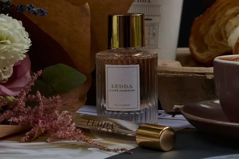 Café Josephine perfume bottle with a gold cap placed on a cozy table with flowers, coffee, and pastries.