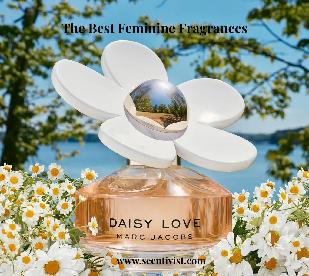 The best feminine fragrances; Marc Jacobs Daisy Love perfume bottle with a white flower cap, surrounded by daisies by a lakeside under a blue sky.