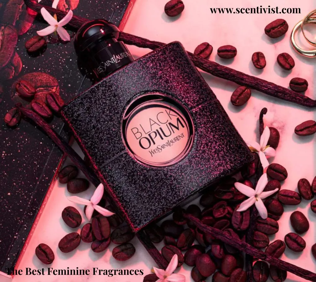 The best feminine fragrances; YSL Black Opium perfume bottle surrounded by coffee beans and delicate white flowers on a pink-toned background.