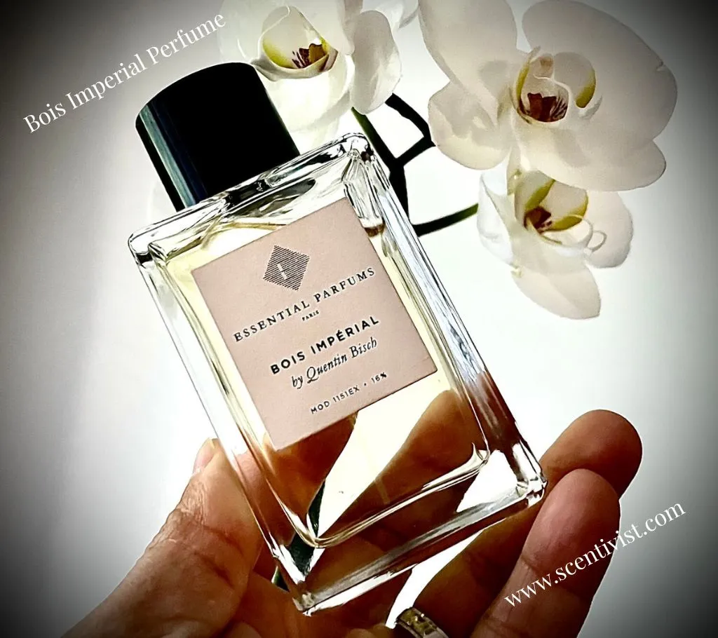 Bois Imperial by Essential Parfums clear glass perfume bottle held in hand with white orchid flowers in the background.