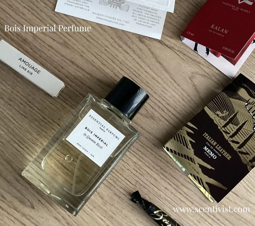 A sleek, square bottle of Bois Imperial perfume rests elegantly on a wooden table, catching the light to highlight its amber-hued liquid.