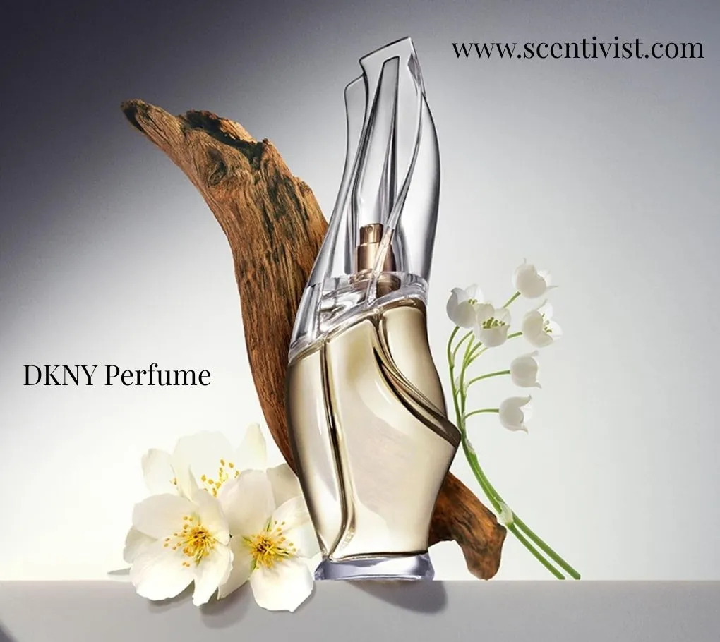 Elegant DKNY perfume bottle with a sculptural glass design, placed beside white flowers and a piece of wood.