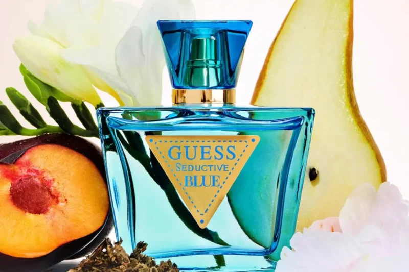 Guess Perfume Seductive Blue bottle in turquoise glass surrounded by pear, peach, flowers, and herbal elements.