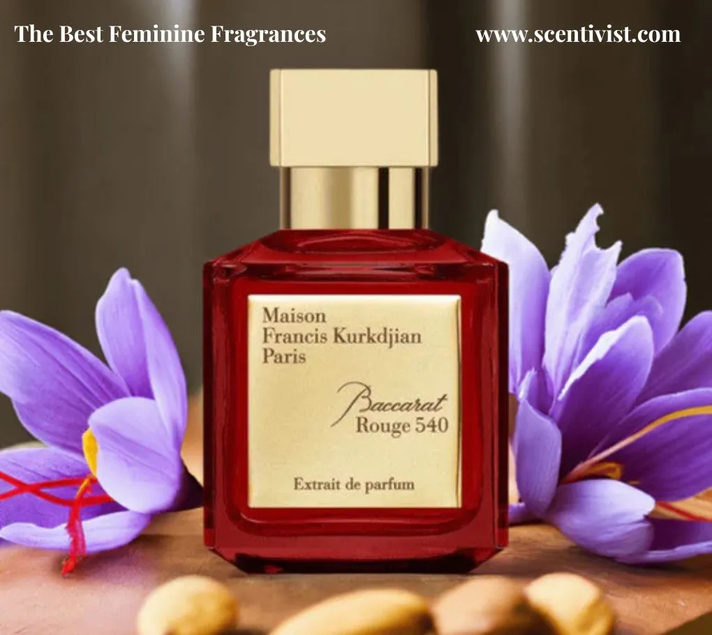 The best feminine fragrance; Maison Francis Kurkdjian Baccarat Rouge 540 perfume bottle with a deep red glass design, placed between purple flowers on a warm-toned surface.